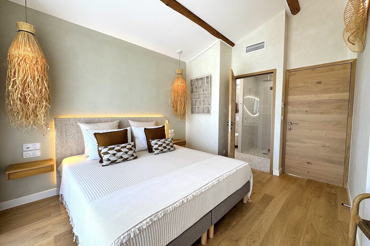 A bedroom with a bed, bedside tables, a shower, and a wooden door.
