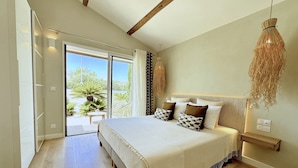 A bedroom with a large bed, a view through the glass door, and a hanging light fixture. - Villa Balāo - Guesthouse Men Only - LGBT (Balaruc-les-Bains)