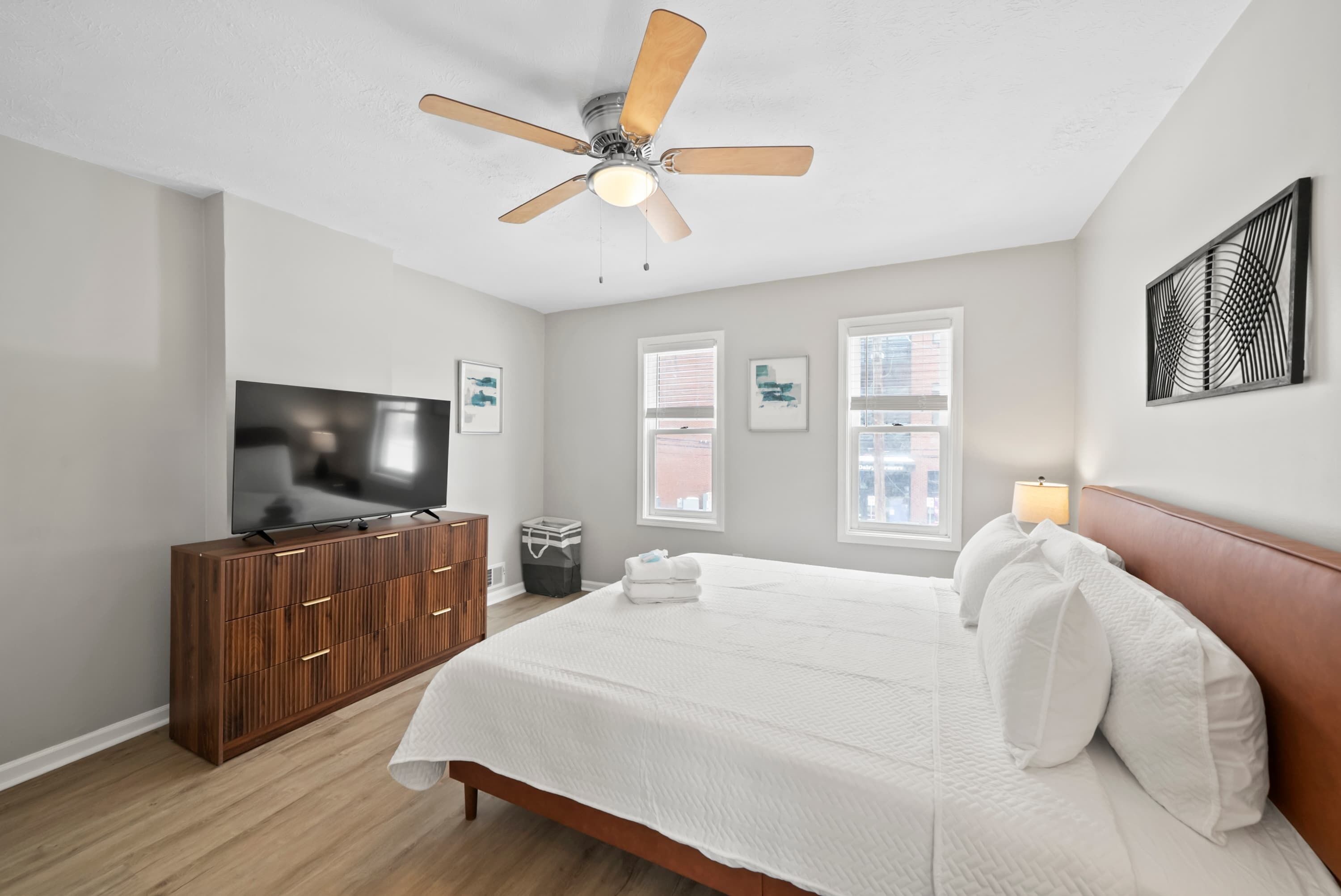 Un dormitorio con cama, televisor, ventilador de techo y ventana.