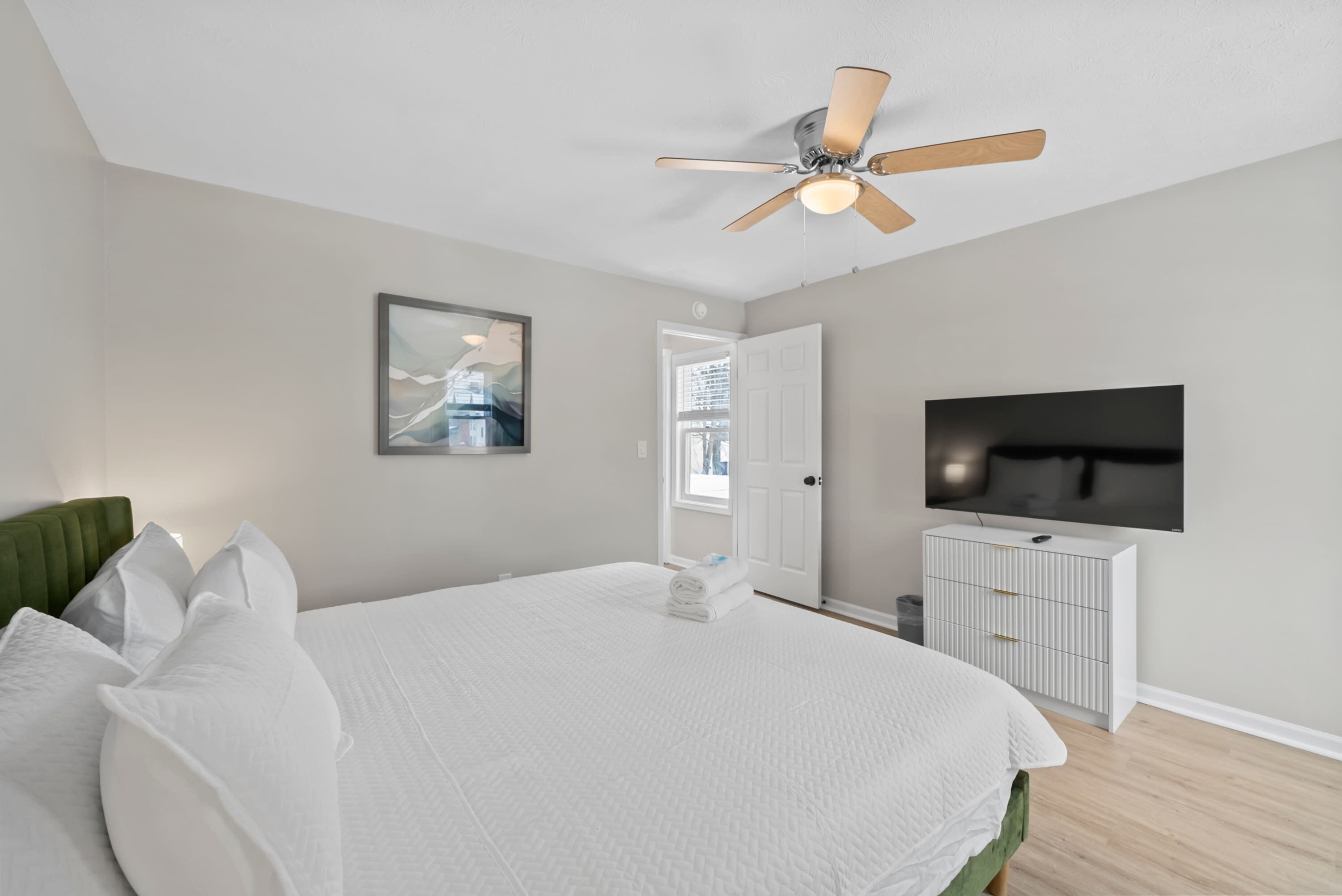 Une chambre avec un grand lit, un ventilateur de plafond, une télévision et une porte donnant sur un balcon.