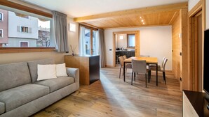 Una sala de estar moderna con sofá, mesa de comedor, sillas, piso de madera y una cocina al fondo.