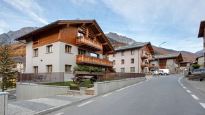 Un edificio moderno con balcones, una calle pavimentada y montañas al fondo.