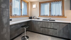 Una cocina moderna con un taburete de bar, dos ventanas con cortinas, un fregadero y una tetera.