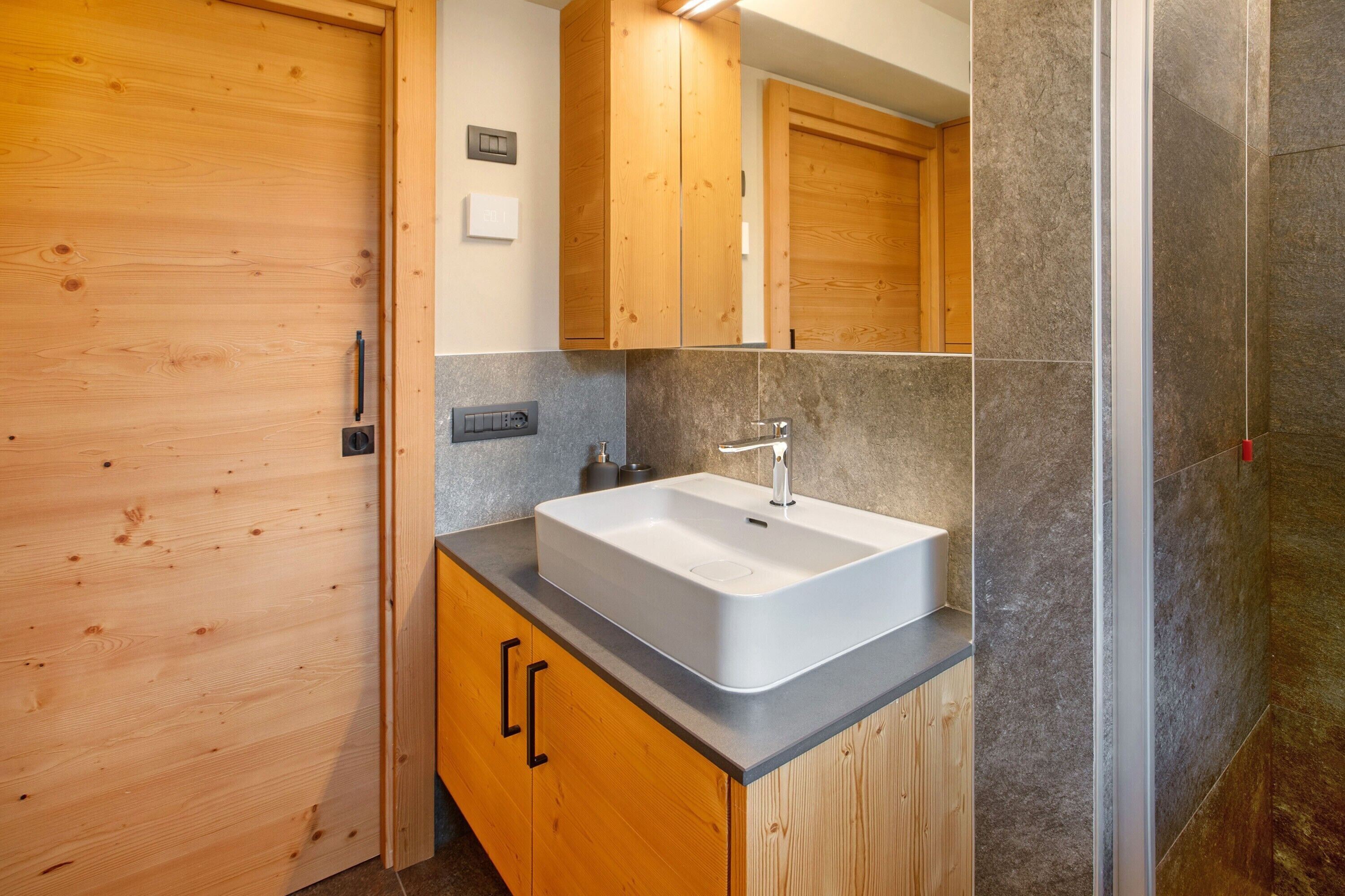 A bathroom with a wooden vanity, a white sink, and a mirror above it.