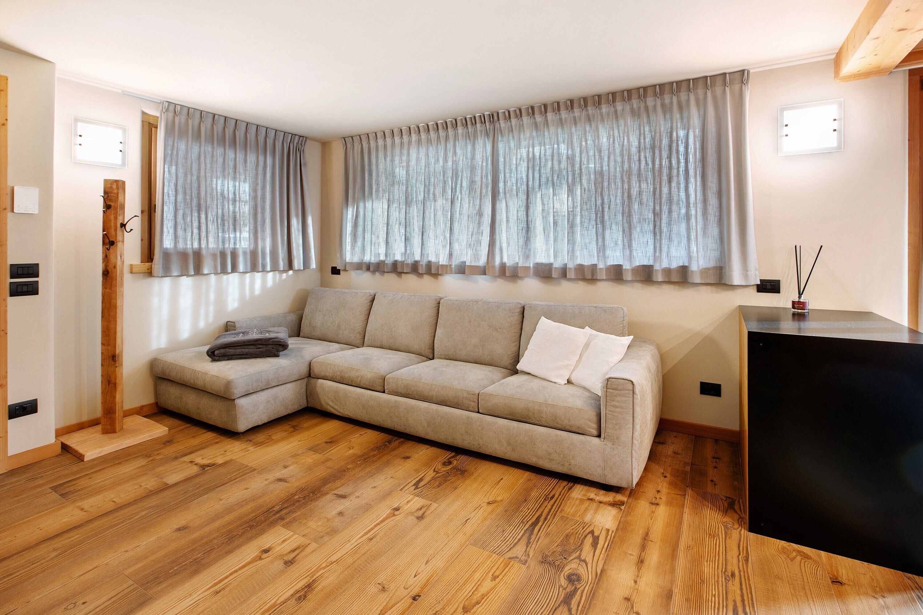 Una sala de estar con sofá modular, piso de madera y un mueble negro.