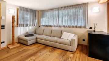 Una sala de estar con sofá modular, piso de madera y un mueble negro.