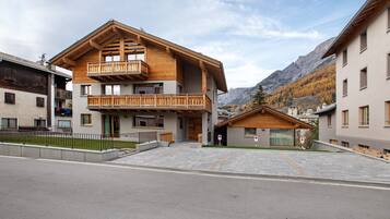 A two-story building with a wooden balcony, a garage, and a mountain backdrop.