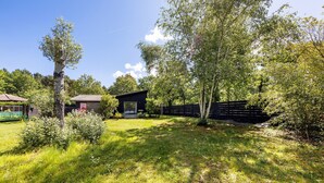 Een huis met een klein terras, een omheinde tuin en een boom op de voorgrond.