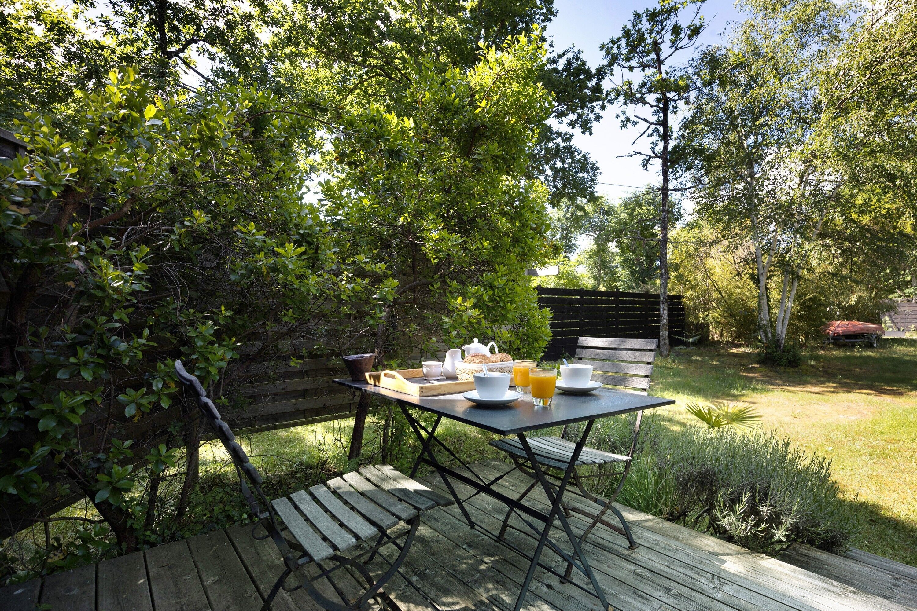 An outdoor wooden deck with a table set for breakfast, surrounded by lush greenery and trees.