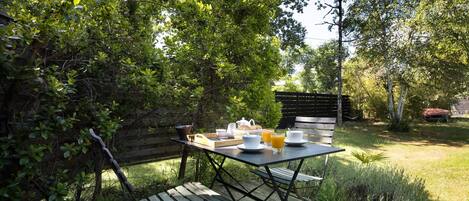 An outdoor wooden deck with a table set for breakfast, surrounded by lush greenery and trees.