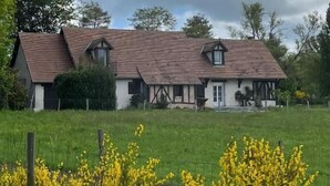 A traditional two-story house with a sloped roof, surrounded by a grassy field and yellow flowering plants. - Oh Fleurs des Champs (Chaumont-sur-Tharonne)