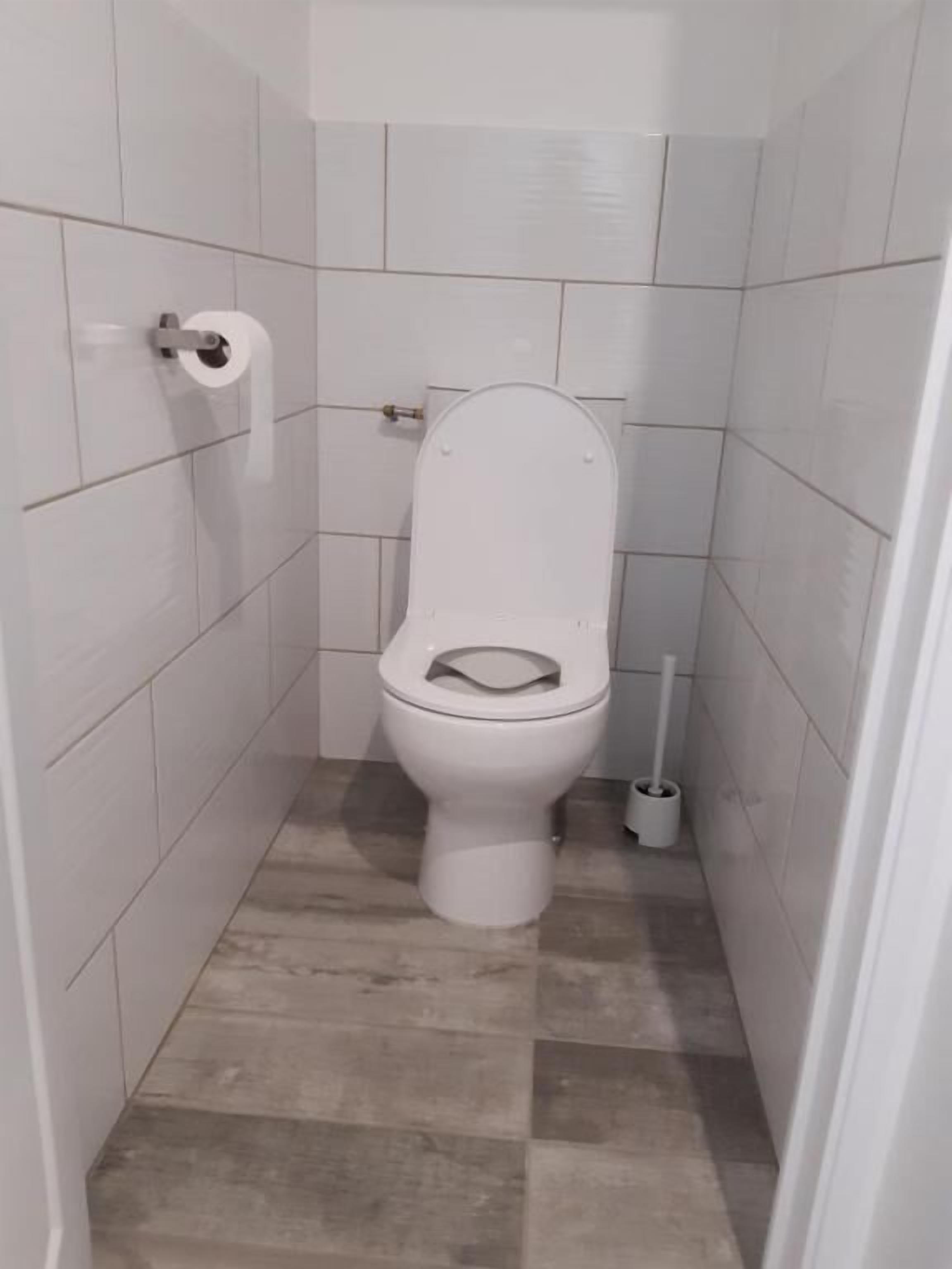 A small, tiled bathroom with a toilet, a toilet paper holder, and a cleaning brush.