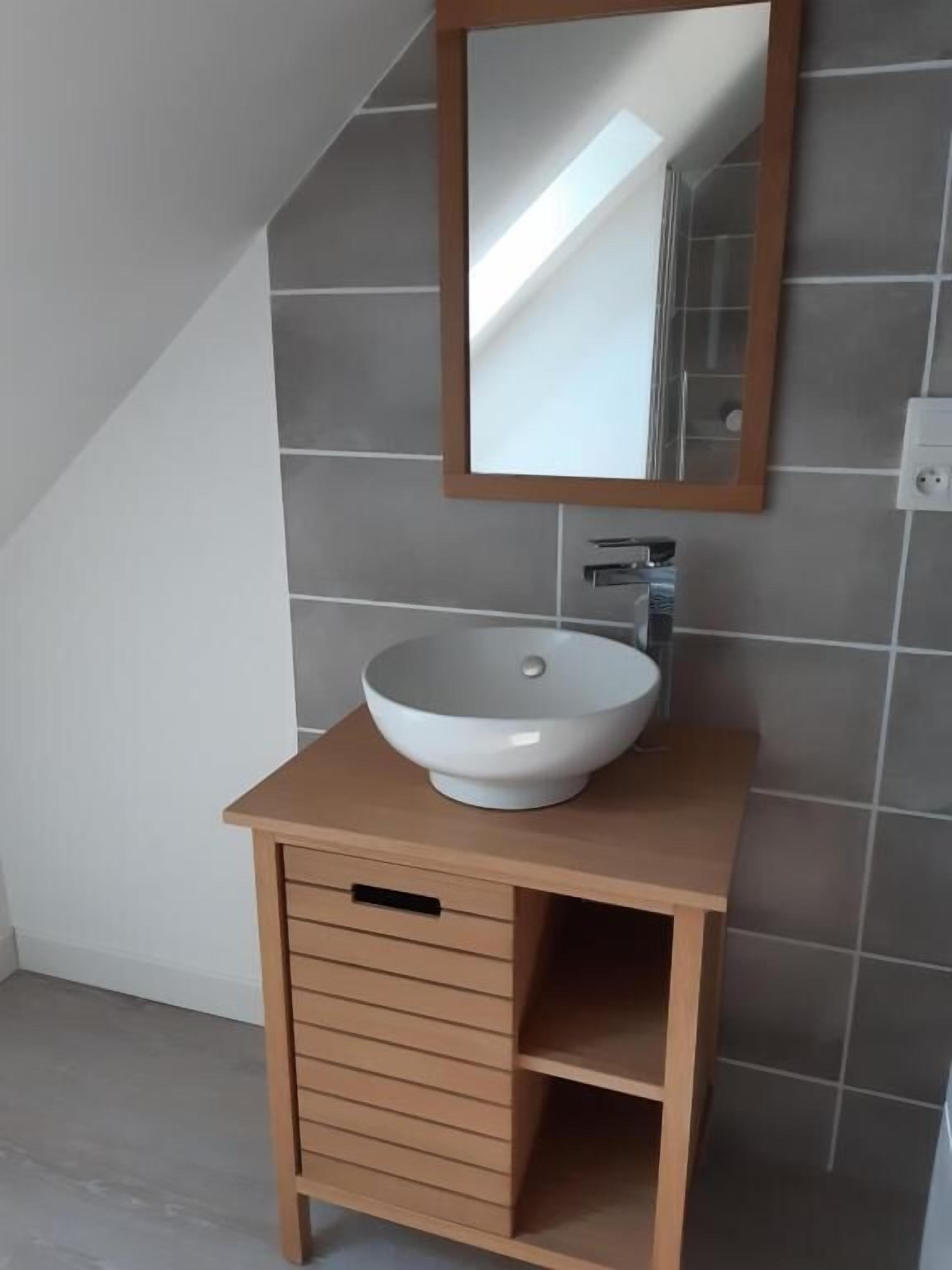 Une salle de bain avec un lavabo blanc, un meuble-lavabo en bois et un miroir au mur.