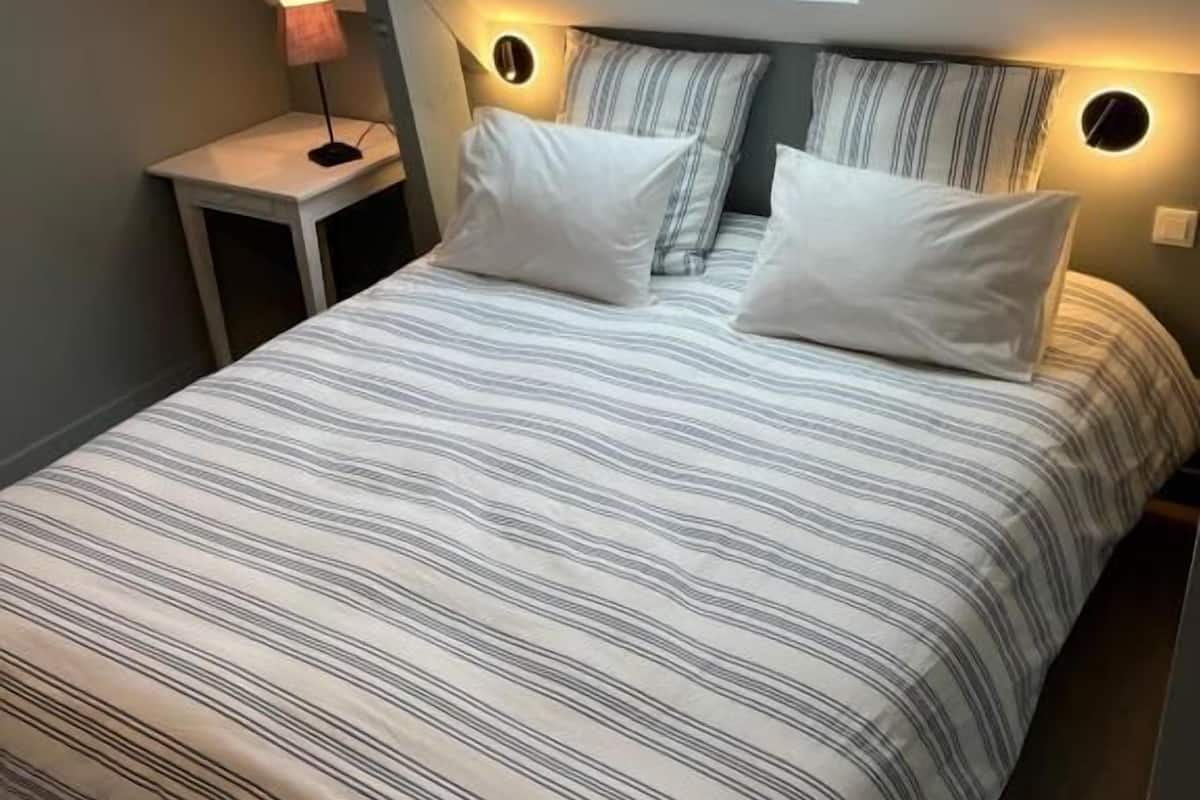 Une chambre avec une lucarne, un lit avec une literie à rayures, des lampes de chevet et une petite table.