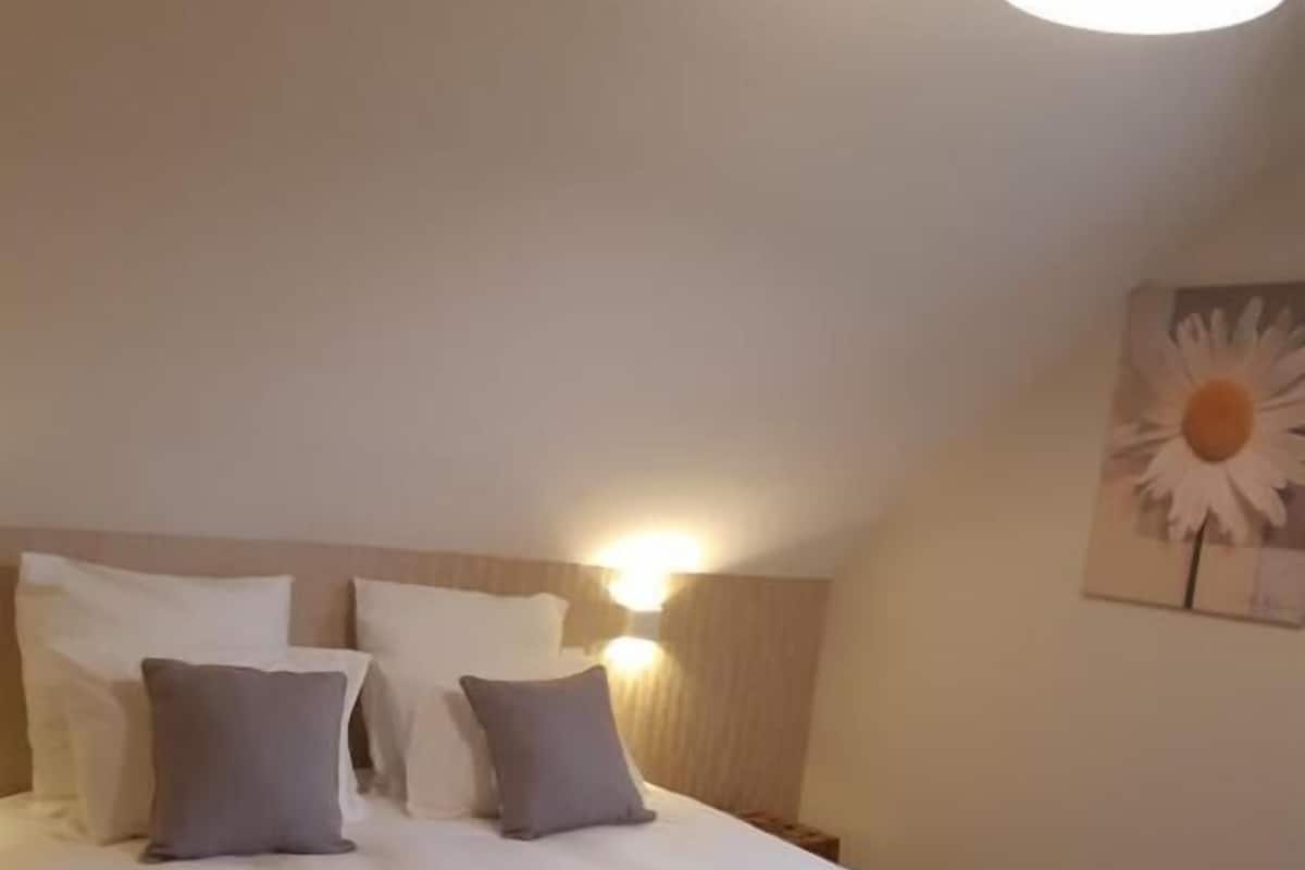 Un lit bien fait, avec une literie blanche et grise, une tête de lit en bois et un luminaire fixé au mur.