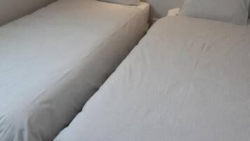 Une chambre avec deux lits simples, un plafond en pente et deux lampes rondes fixées au mur.