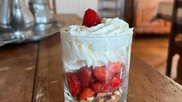 Un postre en una copa de cristal transparente con crema batida y fresas sobre una mesa de madera.