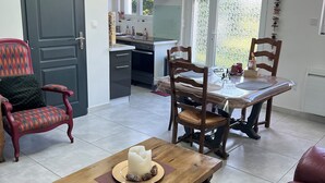 A cozy living room with a wooden coffee table, a red leather sofa, and a dining table with chairs. A kitchen is visible in the background with a window and a door. - Adrien's place! (Châlette-sur-Loing)