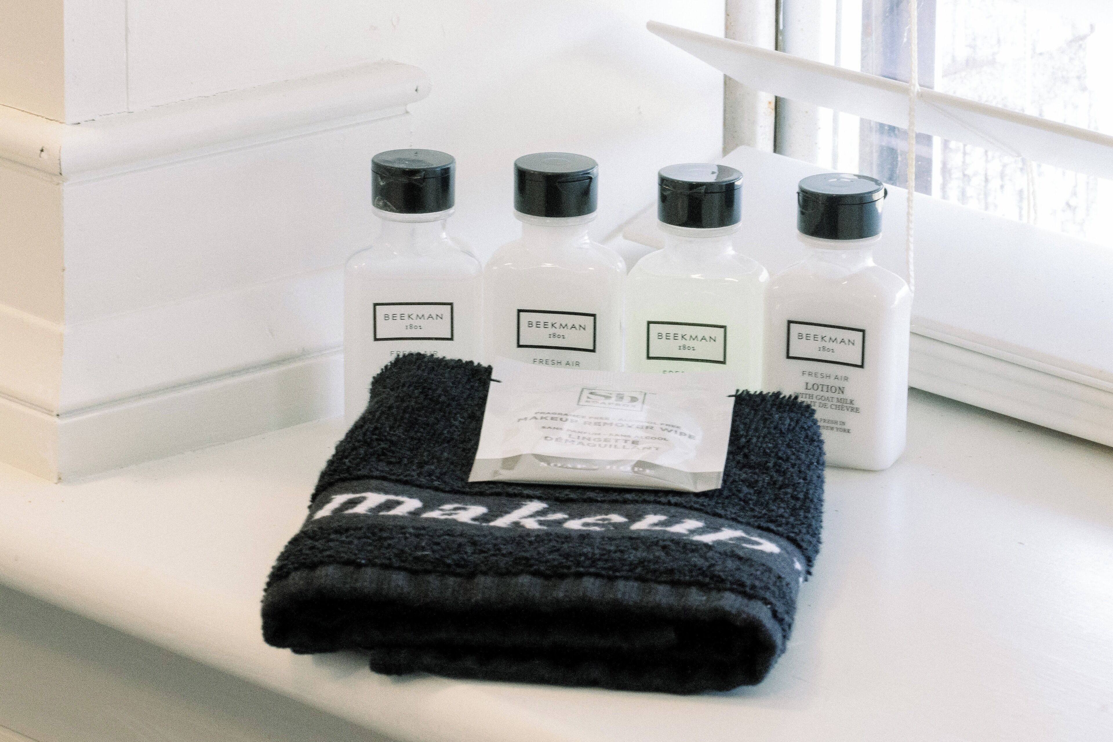 Une salle de bain avec une fenêtre, une serviette et quatre bouteilles de lotion Beekman.