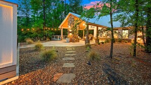 A modern house with a stone exterior, a covered patio, and a well-maintained garden with a stone pathway. - Private Pool with Fenced Dog Yard & Kids Playset (Broken Bow)