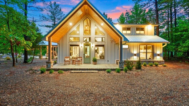 A two-story log cabin with a prominent gable roof, large windows, and a porch with outdoor seating. - Private Pool with Fenced Dog Yard & Kids Playset (Broken Bow)