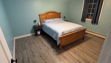 Un dormitorio con una cama de madera, una mesita de noche, un ventilador de techo y una ventana con cortinas.