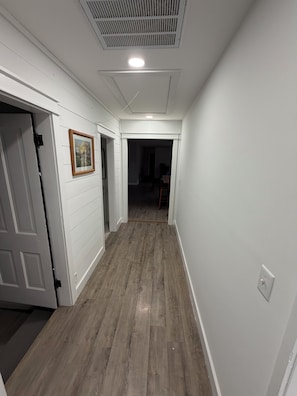 A hallway with white walls, a wooden floor, and a ceiling vent.