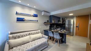 A compact living space with a sofa, dining table, chairs, and a kitchenette. - Flats no Carneiros Atlantico - Proximo da Igrejinha (Tamandaré)