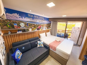 A hotel room with a bed, a sofa, a window with a view, and a wall with a welcome sign and local landmarks. - Flats no Carneiros Atlantico - Proximo da Igrejinha (Tamandaré)