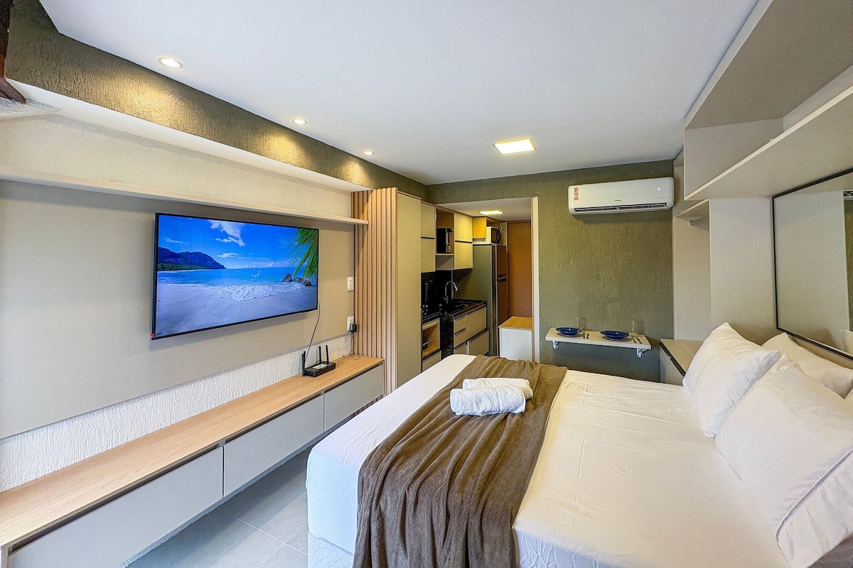 Ein Hotelzimmer mit einem Bett, einem an der Wand befestigten Fernseher, einer kleinen Küchenzeile und einer Klimaanlage.