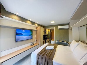 Ein Hotelzimmer mit einem Bett, einem an der Wand befestigten Fernseher, einer kleinen Küchenzeile und einer Klimaanlage.