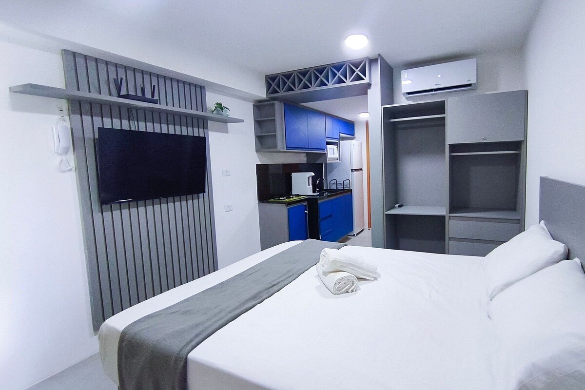 A hotel room with a bed, a TV, a kitchenette, and a wardrobe.