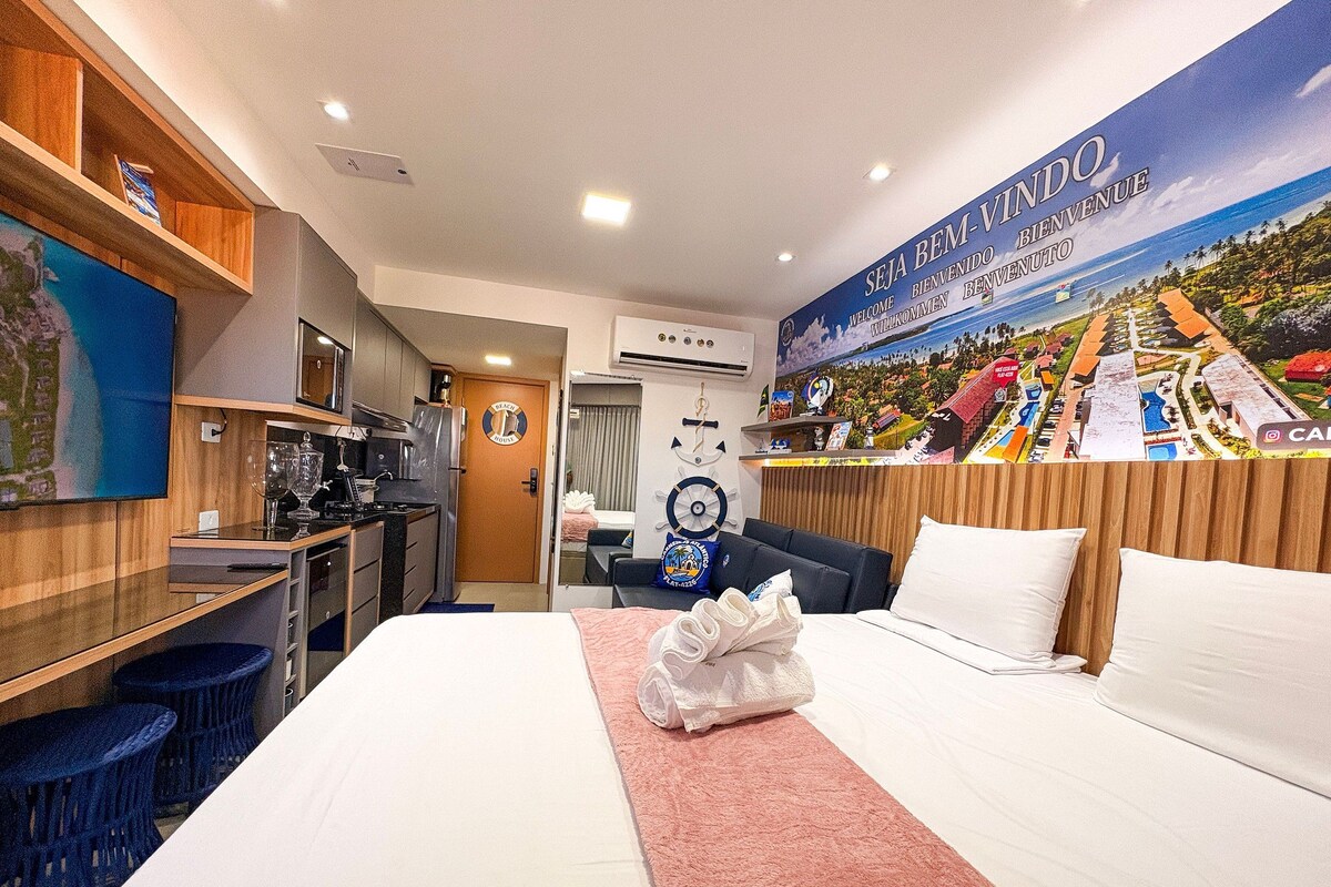 A hotel room with a bed, a desk, a kitchenette, and a bathroom.