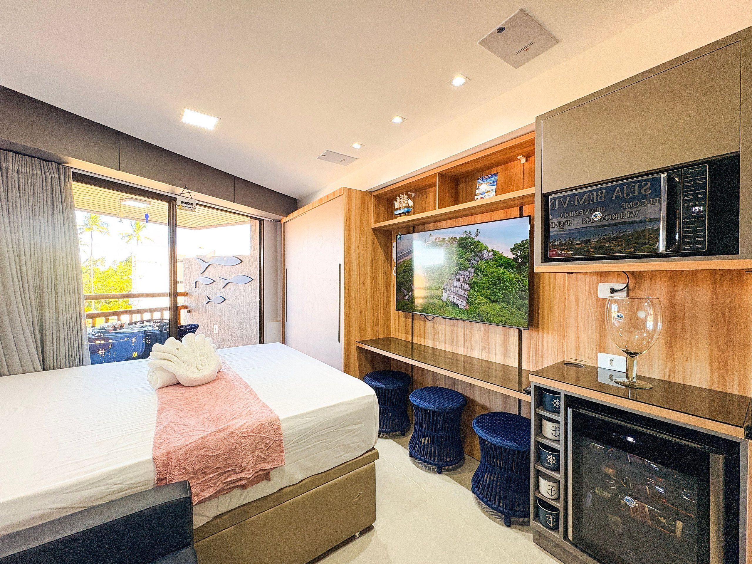 Ein Hotelzimmer mit Bett, Fernseher, Minibar und Blick ins Freie.