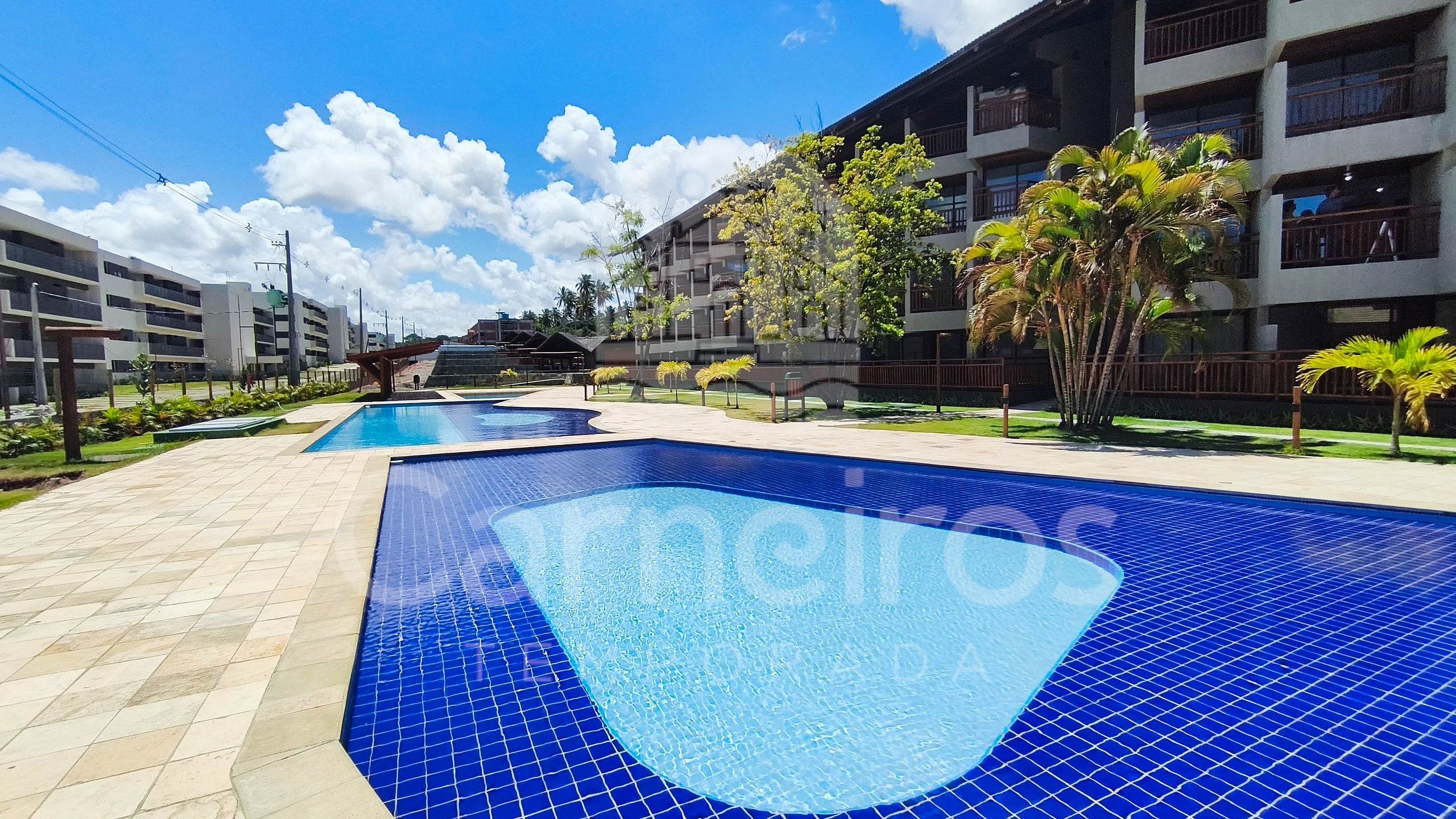 A swimming pool area with multiple pools, surrounded by buildings and palm trees.
