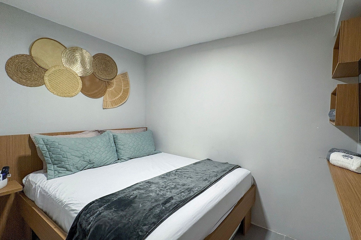 Ein Schlafzimmer mit einem Bett, einem Nachttisch und einem an der Wand befestigten Spiegel.