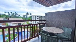 A balcony with a view of a swimming pool and palm trees, a round table, and wicker chairs. - Flats no Carneiros Atlantico - Proximo da Igrejinha (Tamandaré)