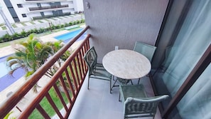 A balcony with a table and chairs, a pool, and a building in the background. - Flats no Carneiros Atlantico - Proximo da Igrejinha (Tamandaré)