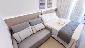 A modern hotel room with a sofa bed, a separate bed, and a view of the sea through the window. - Flats no Carneiros Atlantico - Proximo da Igrejinha (Tamandaré)