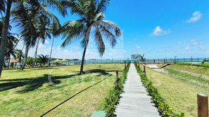 A pathway leading to a beach with palm trees, a thatched-roof structure, and a clear view of the sea. - Flats no Carneiros Atlantico - Proximo da Igrejinha (Tamandaré)