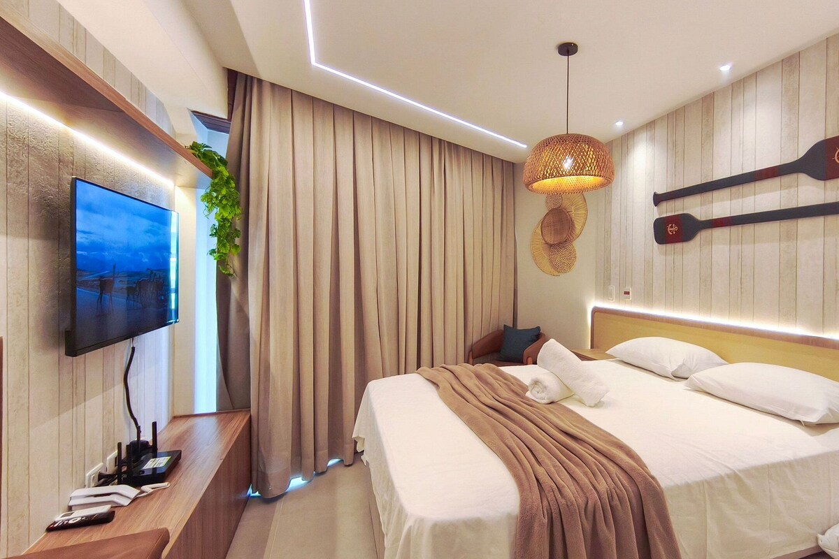 A modern hotel room with a large bed, a flat-screen TV, a wall-mounted paddleboard, and a hanging light fixture.