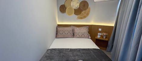 Une chambre d’hôtel avec un lit, une table de chevet, un climatiseur fixé au mur et un rideau.