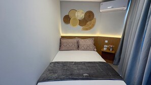 A hotel room with a bed, a nightstand, a wall-mounted air conditioner, and a curtain. - Flats no Carneiros Atlantico - Proximo da Igrejinha (Tamandaré)