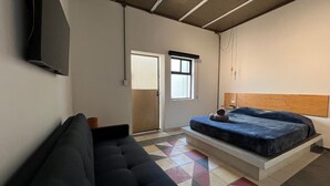 Een kamer met een bed, een slaapbank, een televisie en een raam.