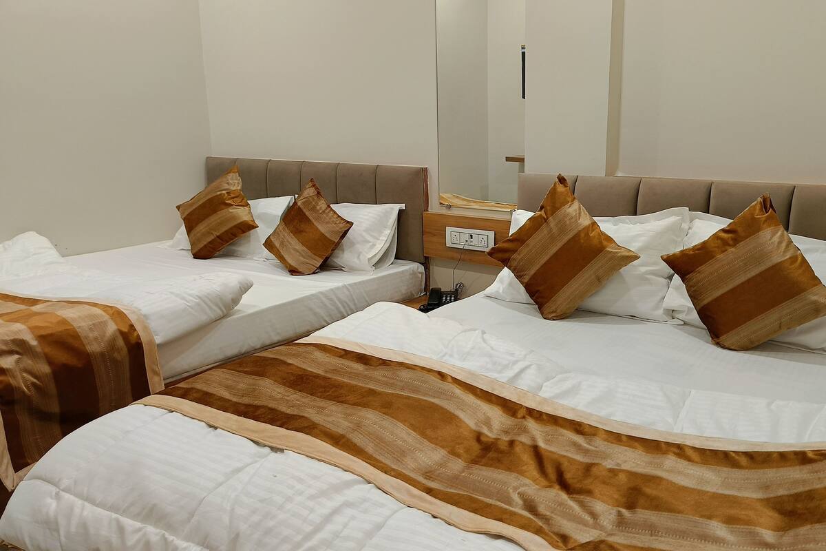 Une chambre d’hôtel avec deux lits, chacun doté de draps blancs et de couvertures à rayures marron. On y trouve une tête de lit en bois, une table de chevet avec un téléphone et une prise électrique fixée au mur.