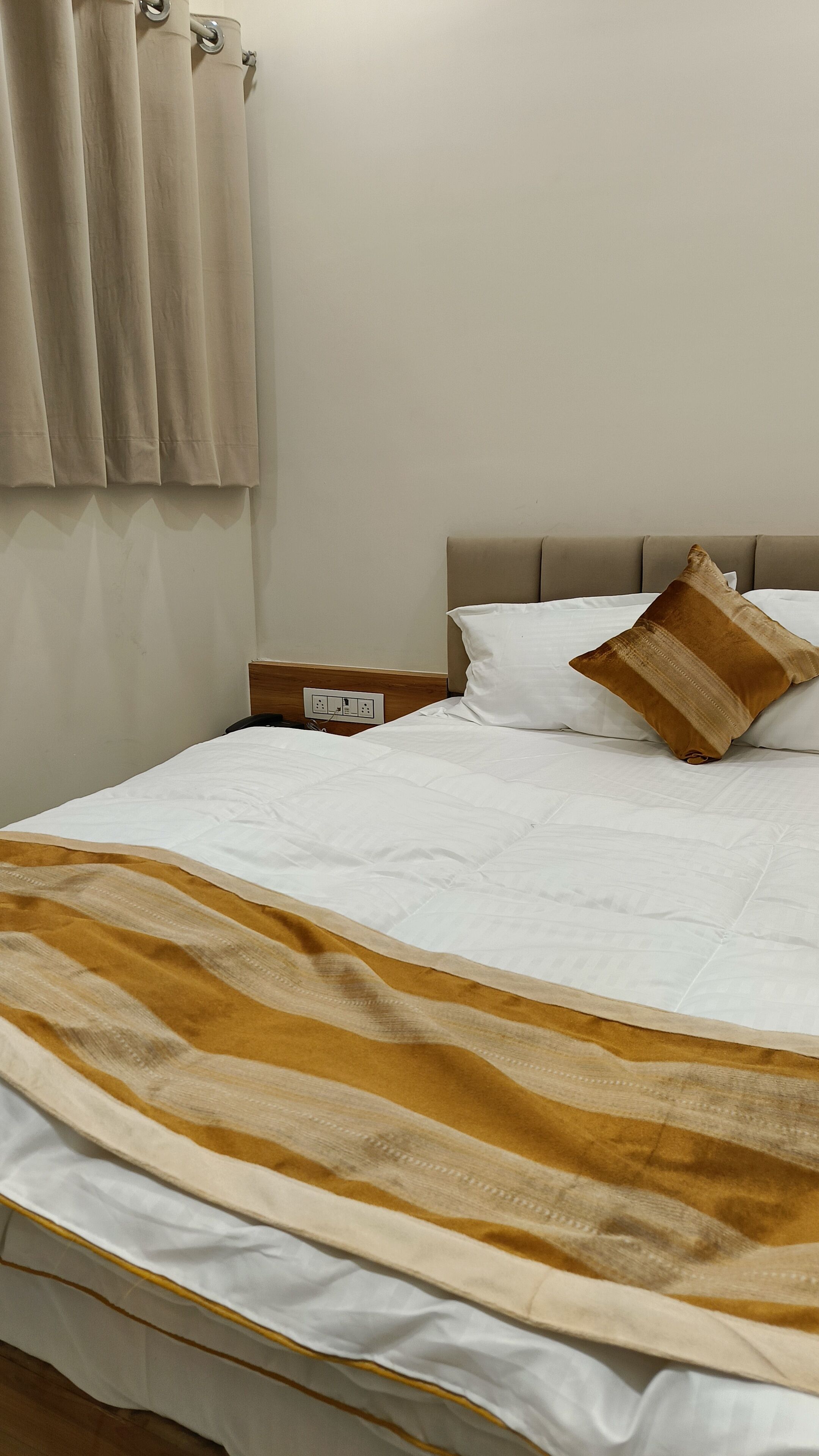 Un lit bien fait, recouvert d’une couverture à rayures, une table de chevet en bois avec un téléphone et une prise électrique au mur.