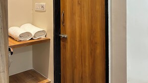 A wooden door with a handle, a towel rack with two towels, and a light switch on the wall. - Shree ShyamRaj Hotel (Ujjain)