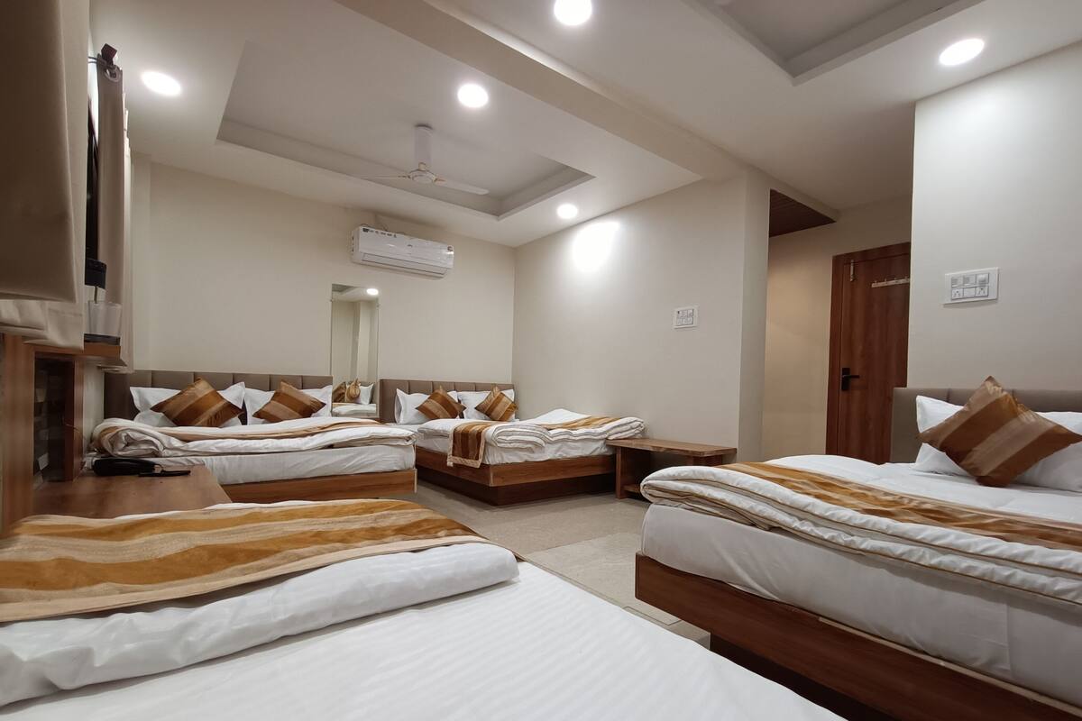 Une chambre d’hôtel avec trois lits, un ventilateur de plafond, un appareil de climatisation et une armoire en bois.