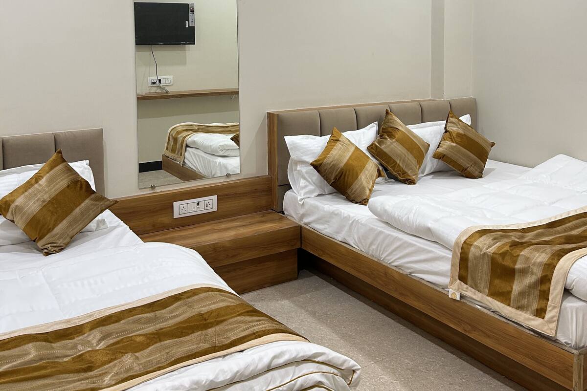 Une chambre d’hôtel avec deux lits, des têtes de lit en bois, un téléviseur à écran plat fixé au mur et une petite étagère avec une prise de courant.