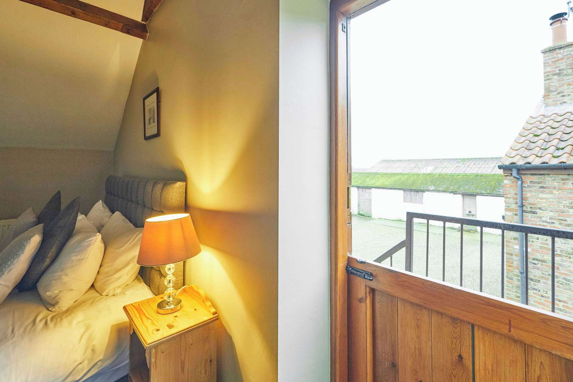 A bedroom with a bed, pillows, a bedside lamp, and a view of a brick building through a window.